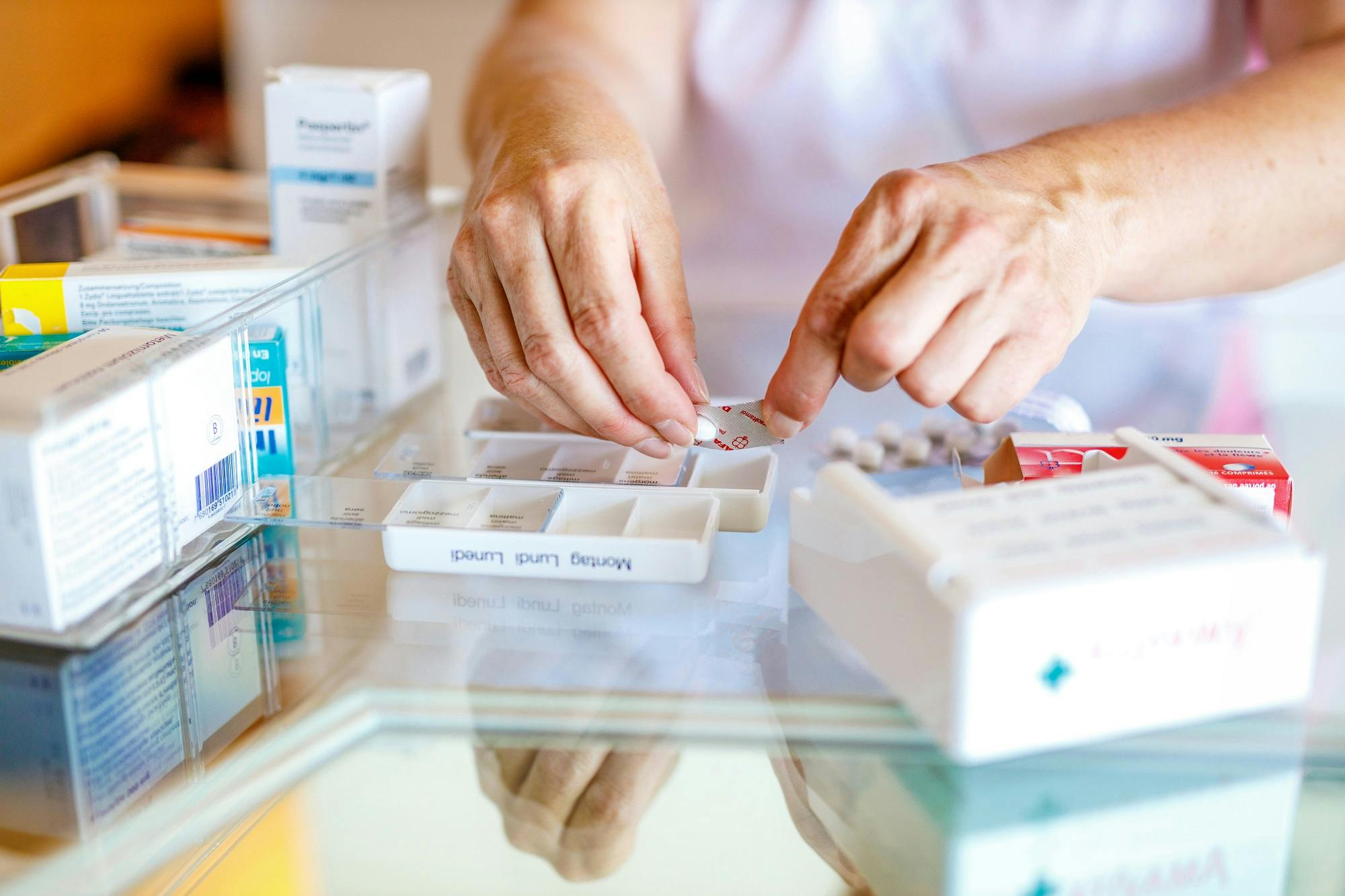 Eine Person sortiert Medikamente in eine Dosierhilfe für die Wochentage.