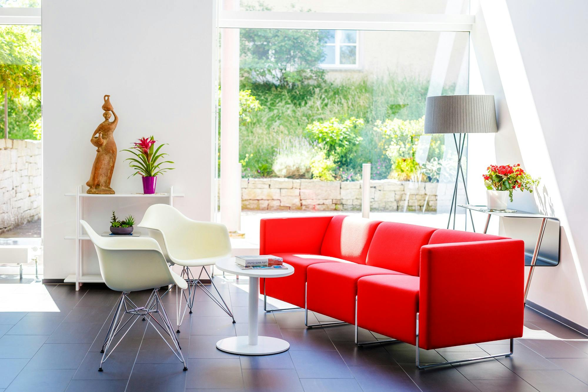 Helles Wohnzimmer mit rotem Sofa, weißem Stuhl und moderner Einrichtung.